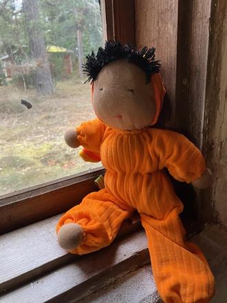 Stor orange kramdocka med randig luva, svart hår och mörk hy