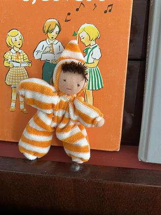 Fickdocka i orange/vitrandig velour med luva, mörk lugg och mörk hy