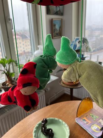 * En knoppdocka har mossgrön kropp och granskottsgrön luva håller i en guldkula