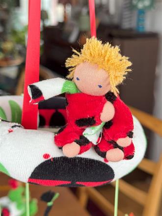 Sittdockan i röd velour med svarta prickar, snuttefilt i samma velour som ringen samt rågblont rakt hår..